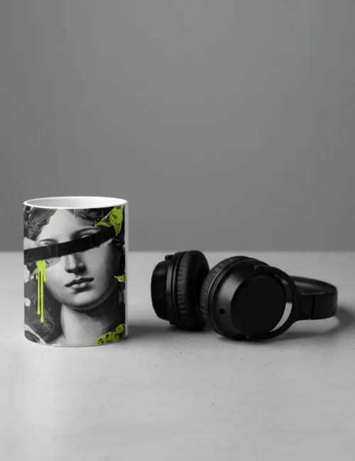 Detail of a hand picking up the neon green collage mug next to a stack of art books and a laptop